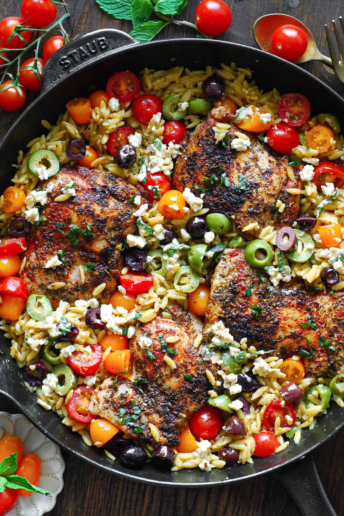 Greek Chicken Orzo with cherry tomatoes and olives - in a cast iron skillet.