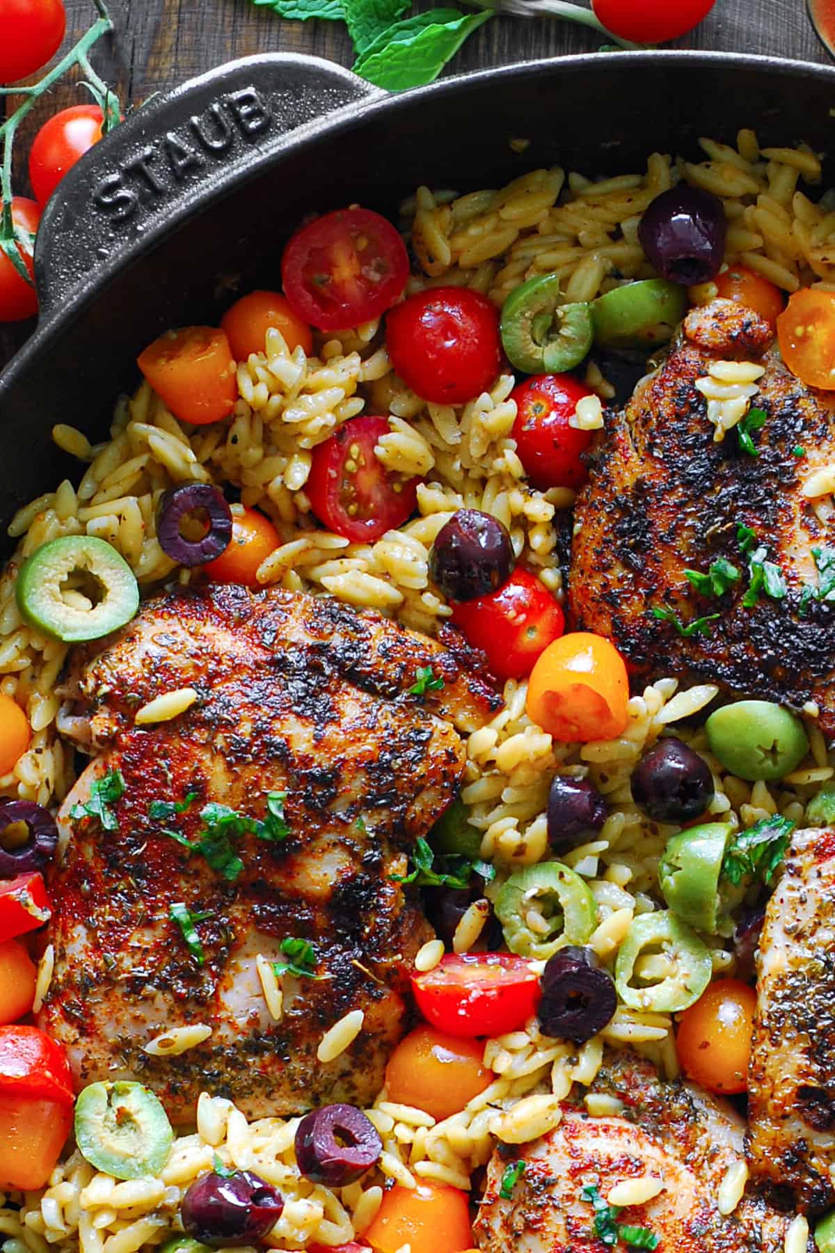 Greek Chicken Orzo with cherry tomatoes and olives - in a cast iron skillet.