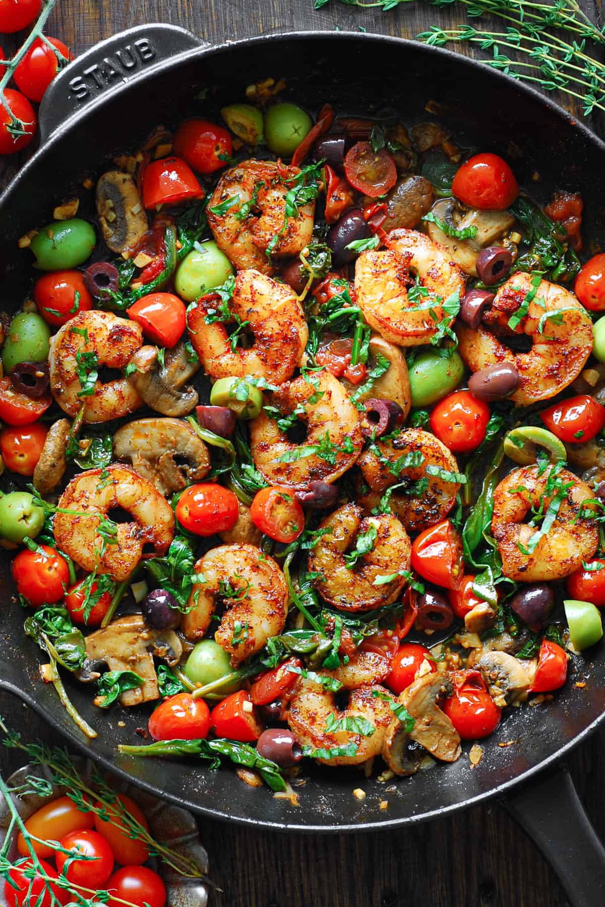 Mediterranean shrimp with olives, cherry tomatoes, garlic, mushrooms, spinach, and a white wine sauce - in a cast iron skillet.