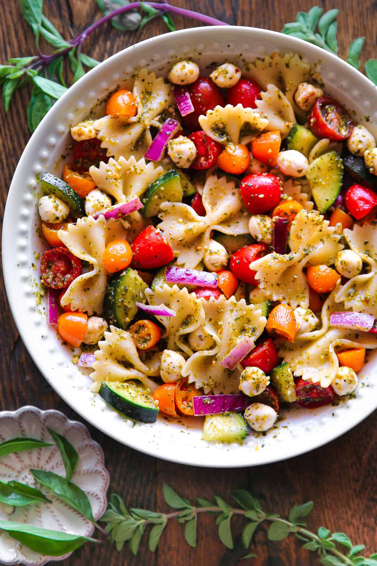 Pesto Pasta Salad with Cherry Tomatoes, Cucumber, Red Onion, and Mozzarella cheese - in a white bowl.