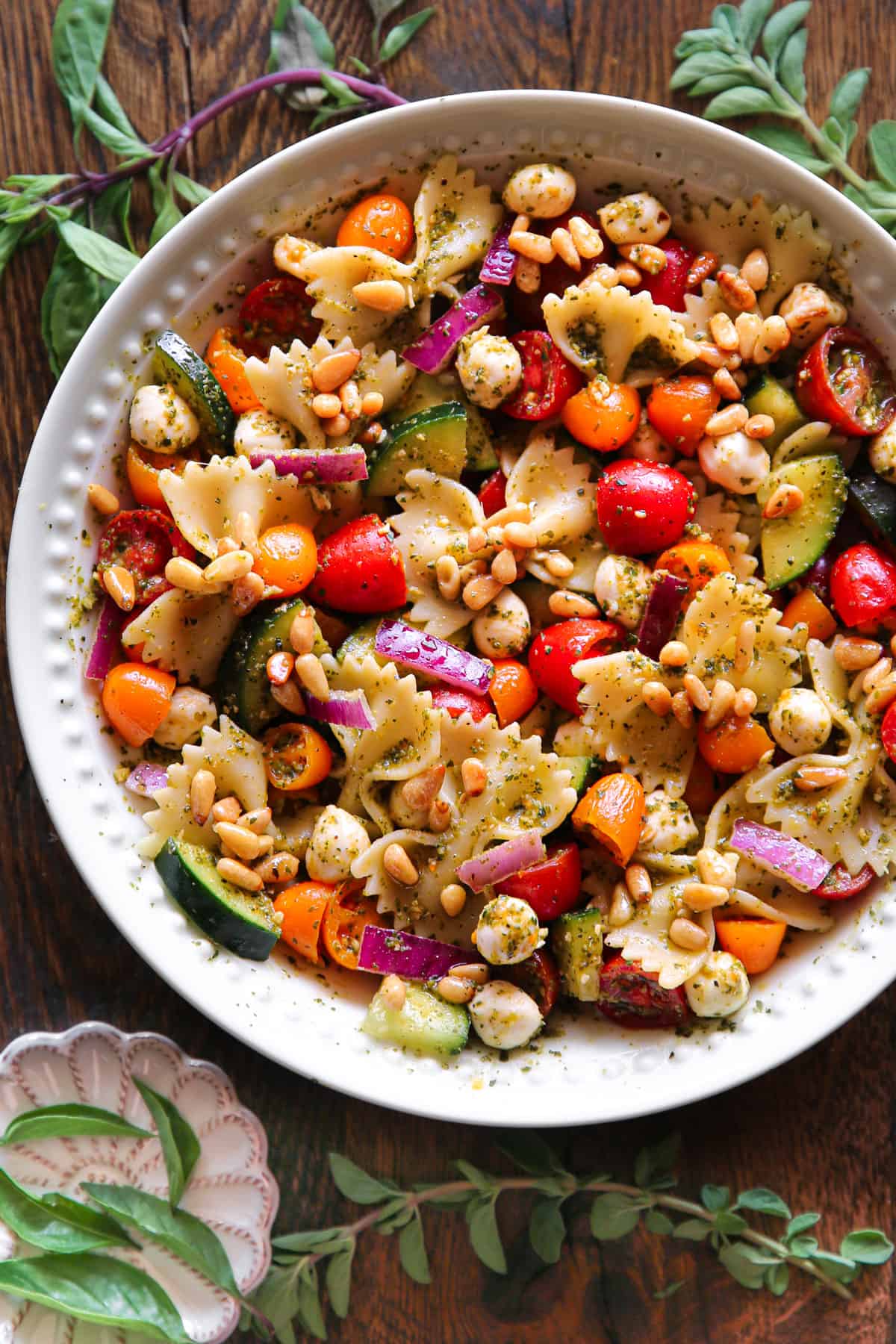 Pesto Pasta Salad with Cherry Tomatoes, Cucumber, Red Onion, Pine Nuts, and Mozzarella cheese - in a white bowl.