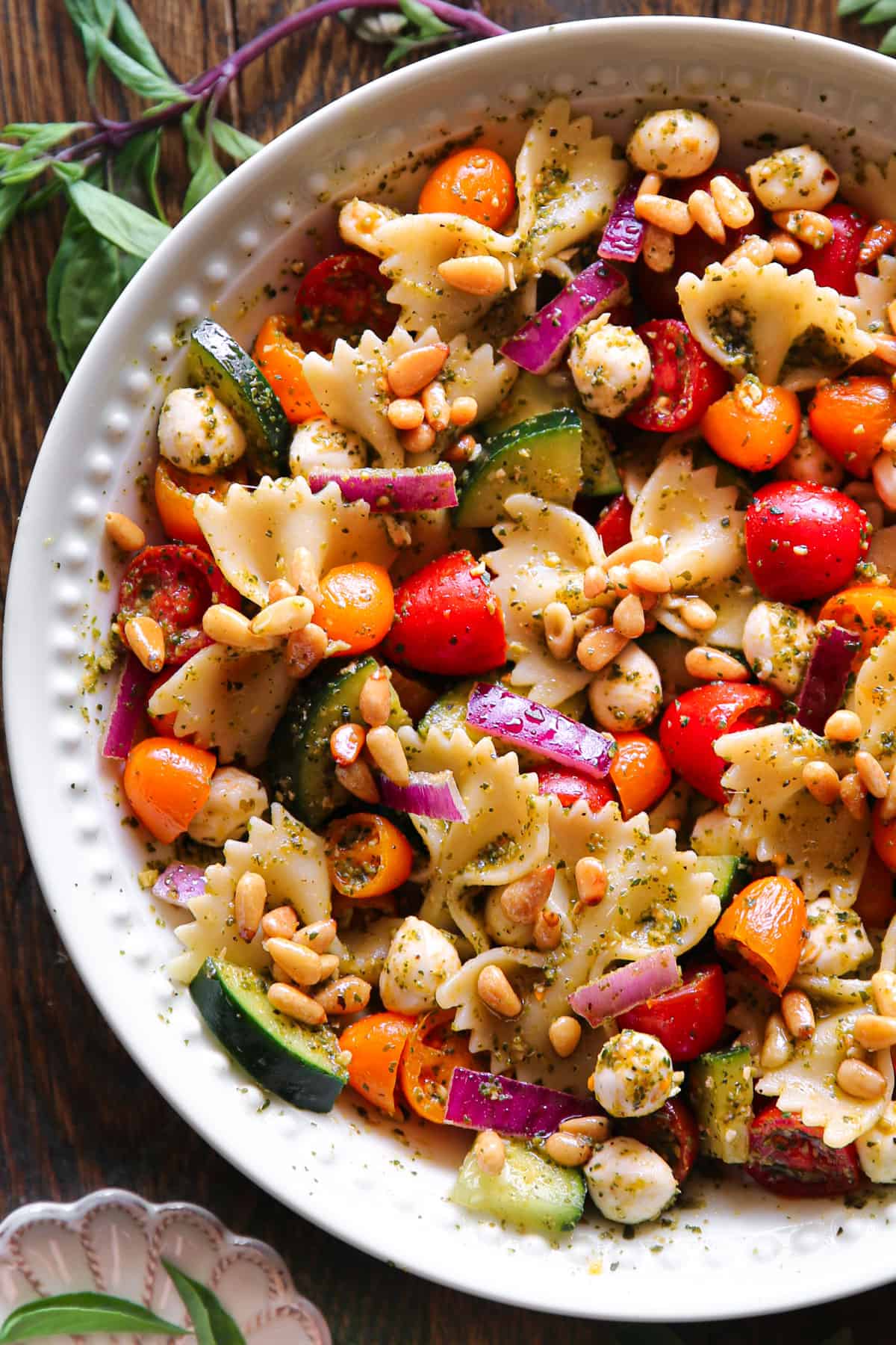 Pesto Pasta Salad with Cherry Tomatoes, Cucumber, Red Onion, Pine Nuts, and Mozzarella cheese - in a white bowl.