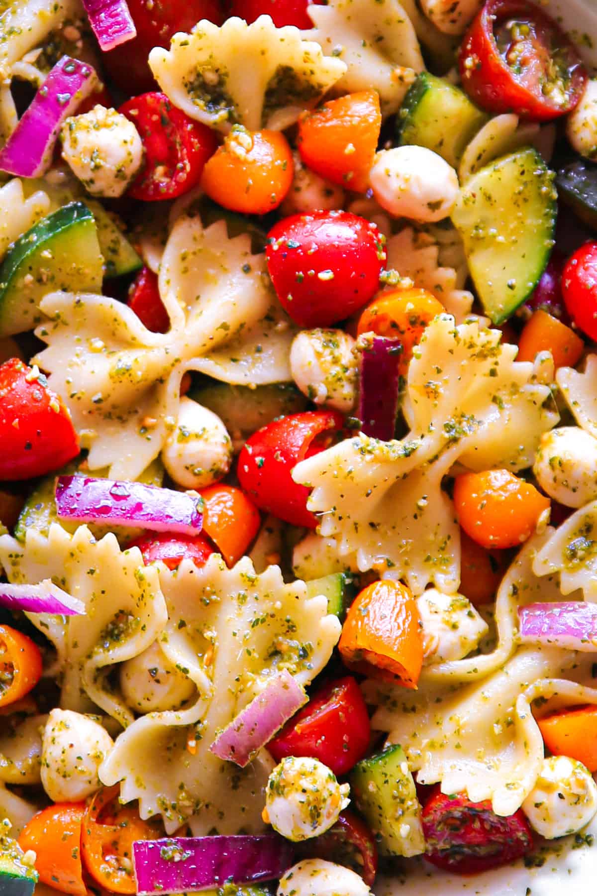 Pesto Pasta Salad with Cherry Tomatoes, Cucumber, Red Onion, and Mozzarella cheese - close-up photo.