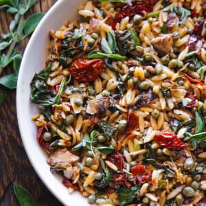 Sun-Dried Tomato and Spinach Orzo with Artichokes and Capers - in a white bowl.