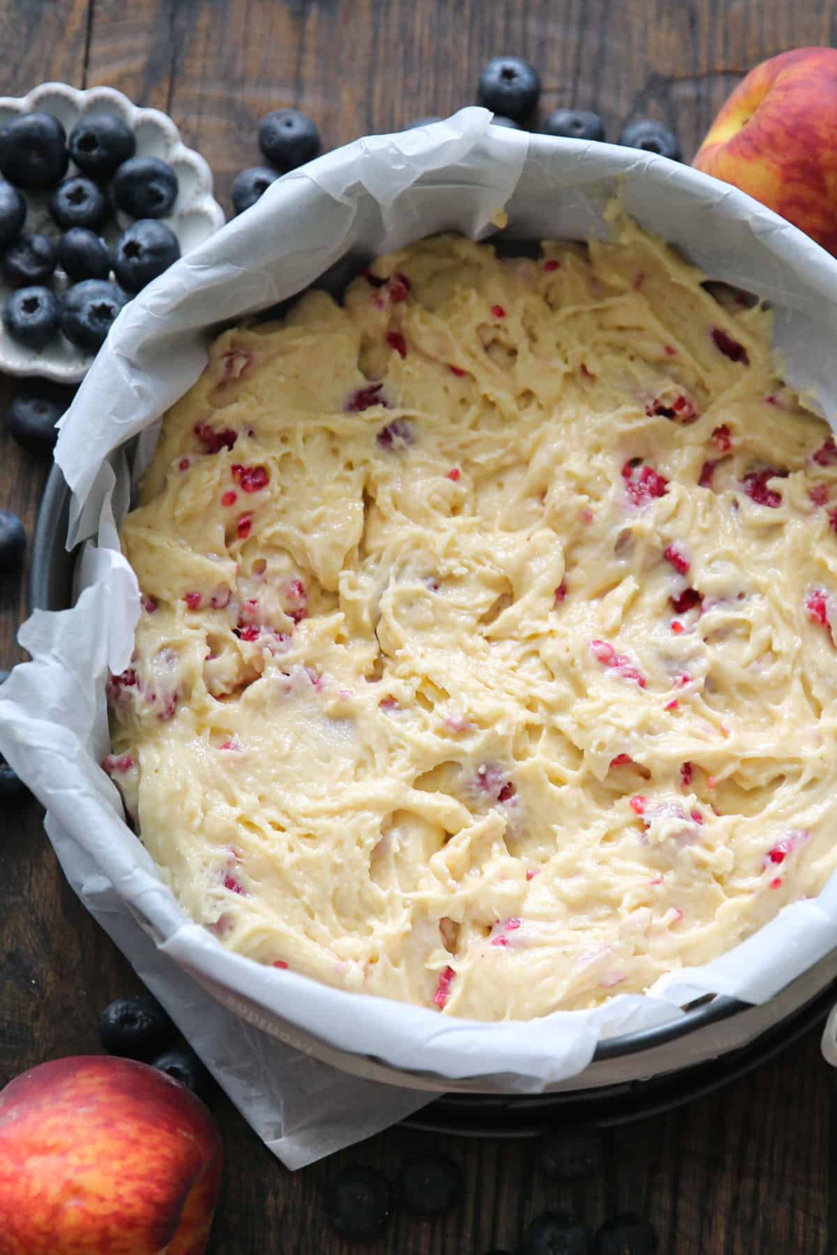 cake batter with folded raspberries in a parchment paper-lined springform baking pan.