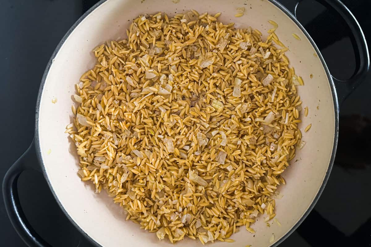 toasted orzo with onions and garlic in a pan.