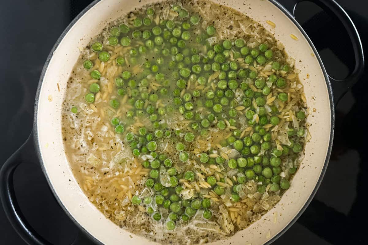 uncooked orzo with fresh green peas and water in a pan.