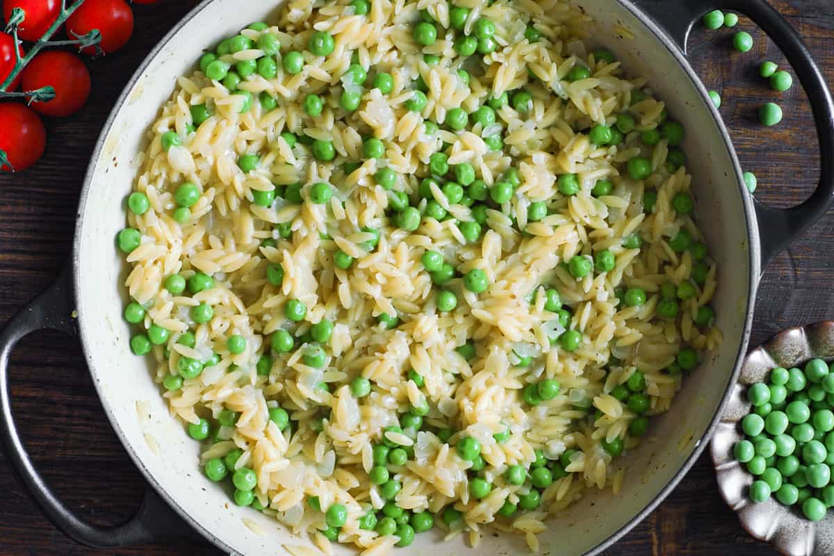 creamy orzo with green peas in a pan.