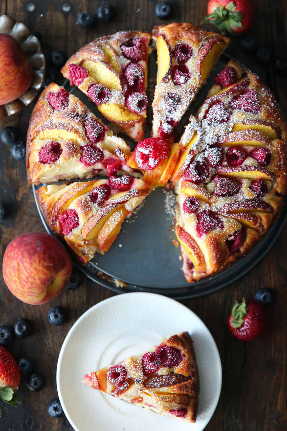 the overhead shot of sliced raspberry peach cake on a cake platter and a slice of cake on a plate.