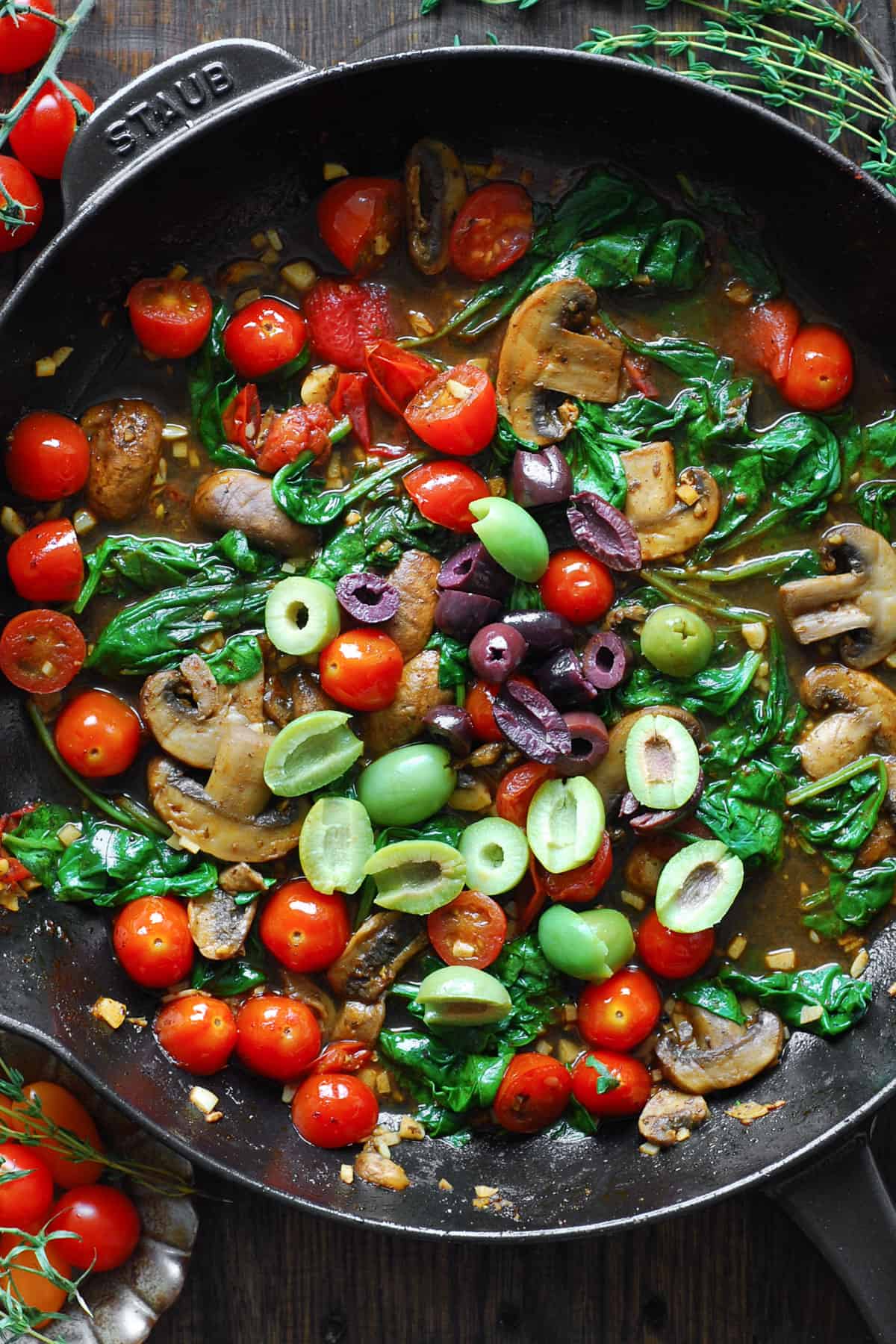 cooked tomatoes, mushrooms, wilted spinach, and sliced olives with white wine sauce in a cast iron skillet.