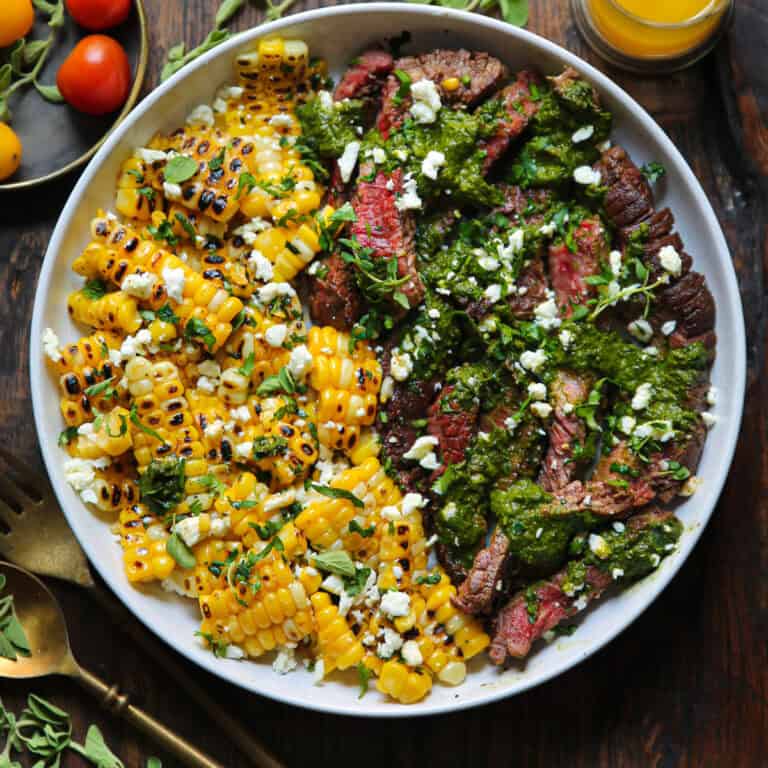 flank steak with corn, spinach sauce, and feta cheese - in a white bowl.