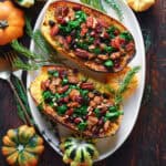 Spaghetti squash stuffed with sausage, spinach, cranberries and walnuts, on a white plate.