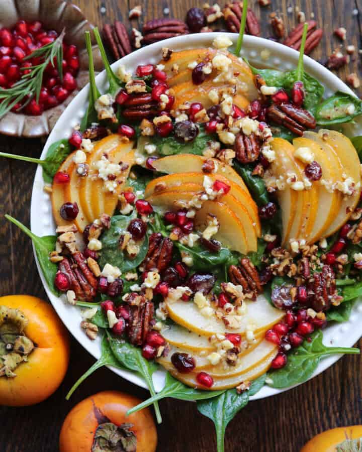 Pear and Pomegranate Spinach Salad with Pecans, Dried Cranberries, Feta Cheese, and Maple-Lemon Mustard Dressing - in a white bowl.