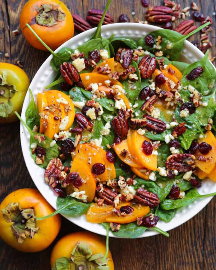 Spinach and Persimmon Salad with Dried Cranberries, Pecans, Feta Cheese, and Honey-Mustard Dressing - in a white bowl.