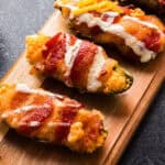 bacon-wrapped jalapeno poppers - on a long wooden board.