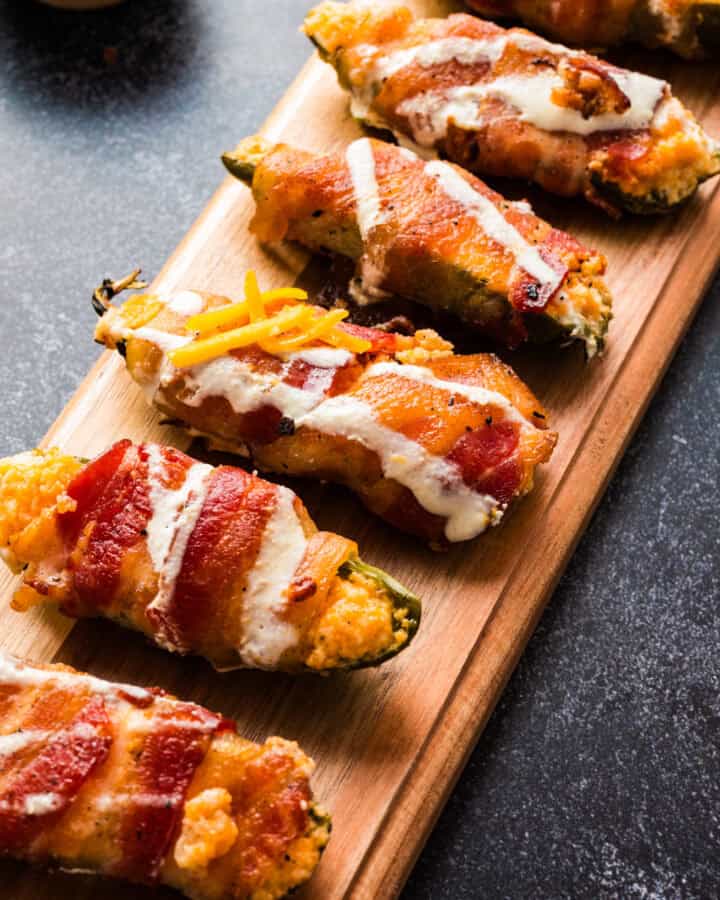 bacon-wrapped jalapeno poppers - on a long wooden board.