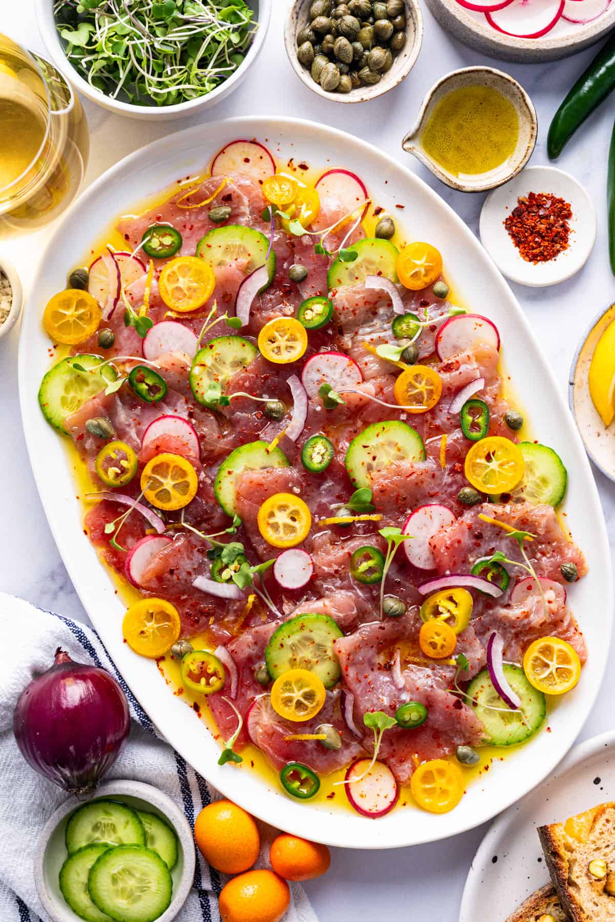 Tuna Crudo Oval platter with thinly sliced raw fish, cucumbers, radishes, kumquats, capers, onions, greens, and chilis.