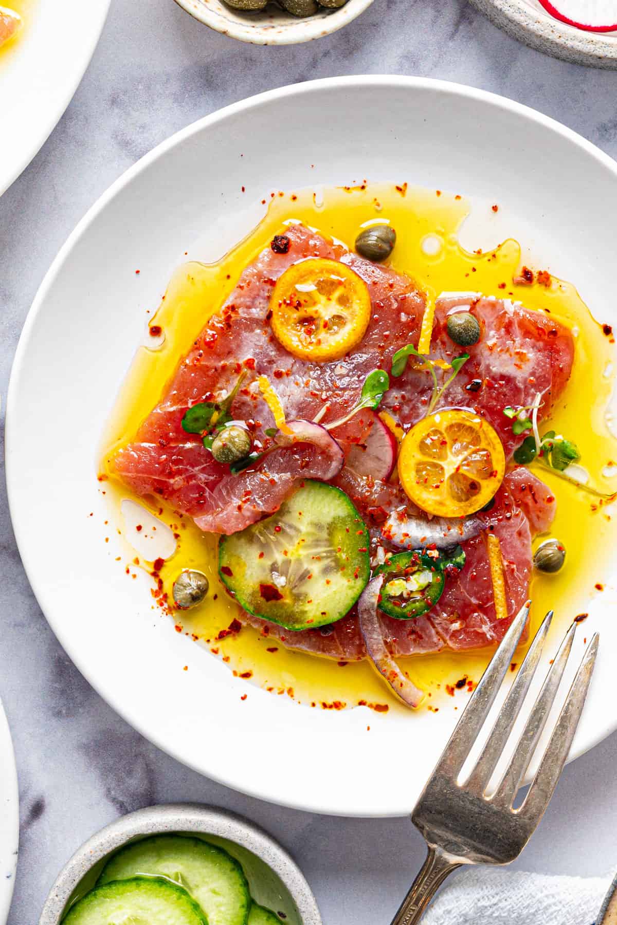 Tuna Crudo Thinly sliced raw tuna with cucumber, kumquat, red onion, microgreens, and chili flakes, drizzled with olive oil.