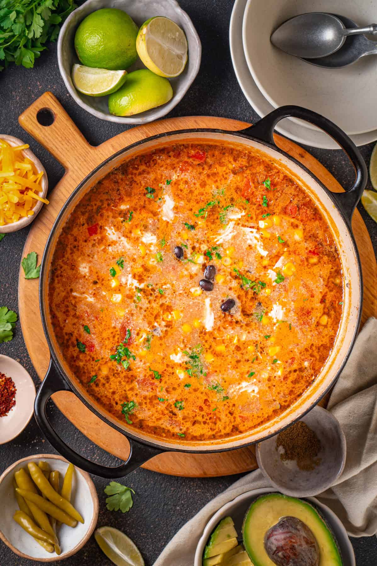 Chicken Enchilada Soup with corn, black beans, green chiles, topped with sliced avocado, Cheddar cheese, and sliced lime - in a dutch oven.