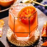 Blood orange margarita on the rocks in a glass with a salted rim.