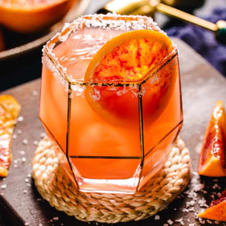 Blood orange margarita on the rocks in a glass with a salted rim.