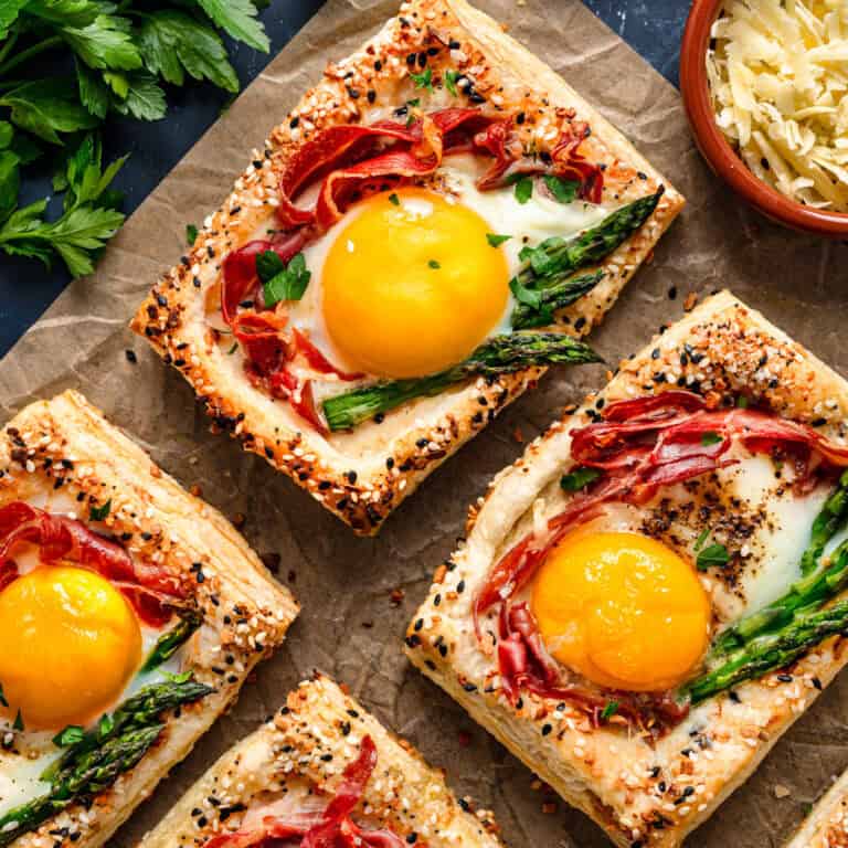 Puff Pastry Egg Tarts topped with asparagus and prosciutto - on parchment paper.