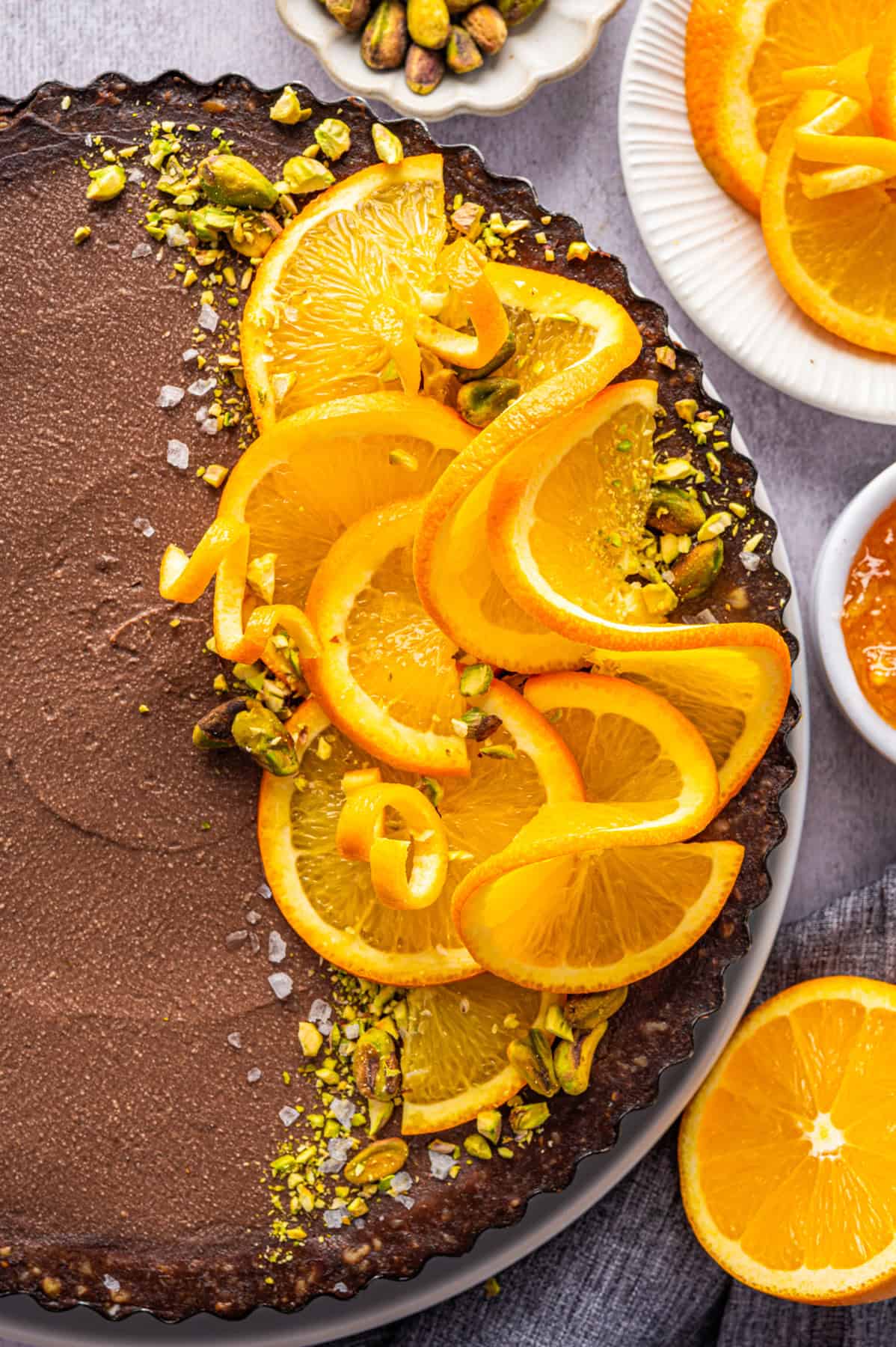 No-Bake Chocolate Tart with Orange Marmalade and Pistachios (Vegan + GF) Chocolate Orange Tart (half of it is topped with fresh orange slices, chopped and whole pistachios, and sea salt).