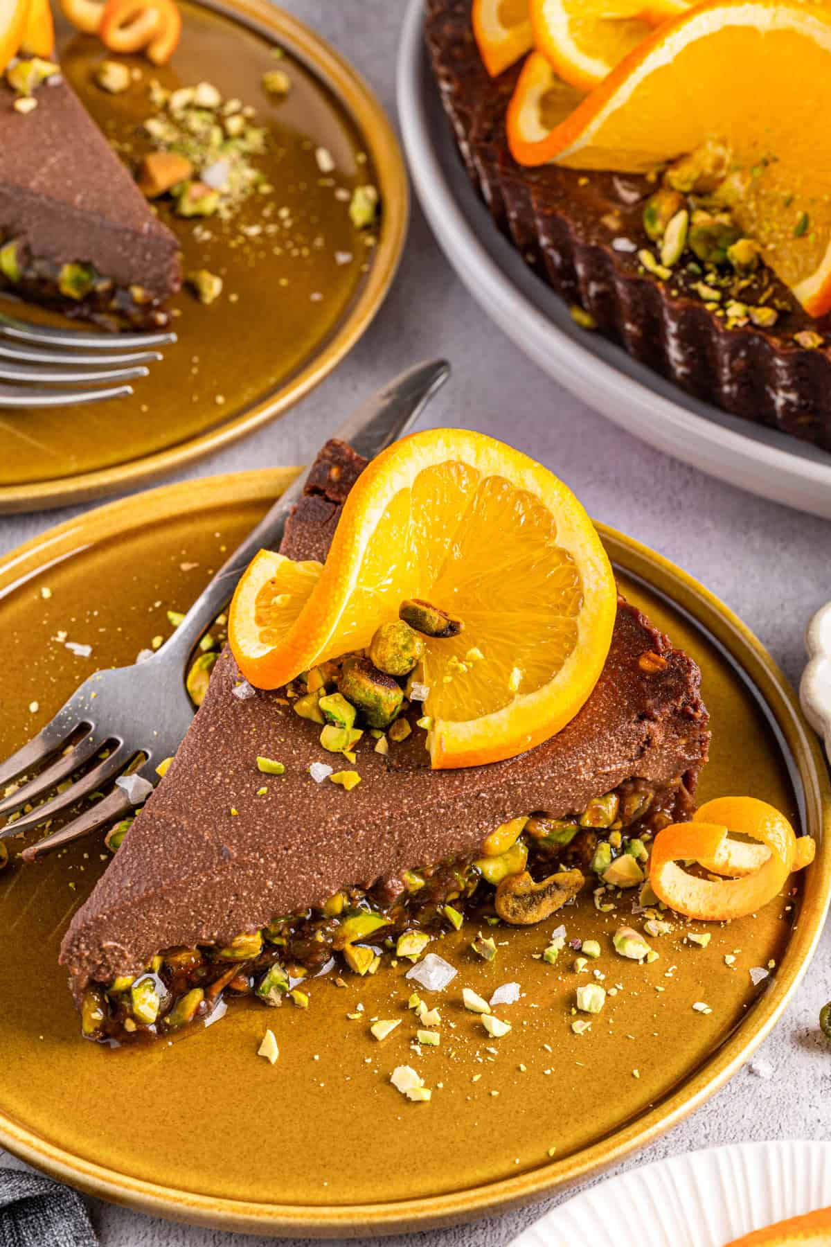 No-Bake Chocolate Tart with Orange Marmalade and Pistachios (Vegan + GF) A slice of Chocolate Orange Tart (topped with fresh orange slices, chopped and whole pistachios, and sea salt) on an orange plate.
