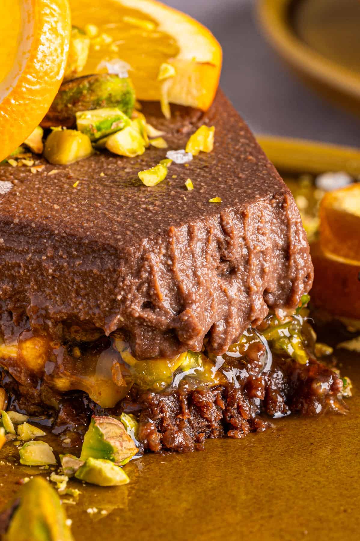 No-Bake Chocolate Tart with Orange Marmalade and Pistachios (Vegan + GF) A close-up photo of a slice of Chocolate Orange Tart on a plate, showcasing the pistachio-orange marmalade and chocolate filling inside the tart.