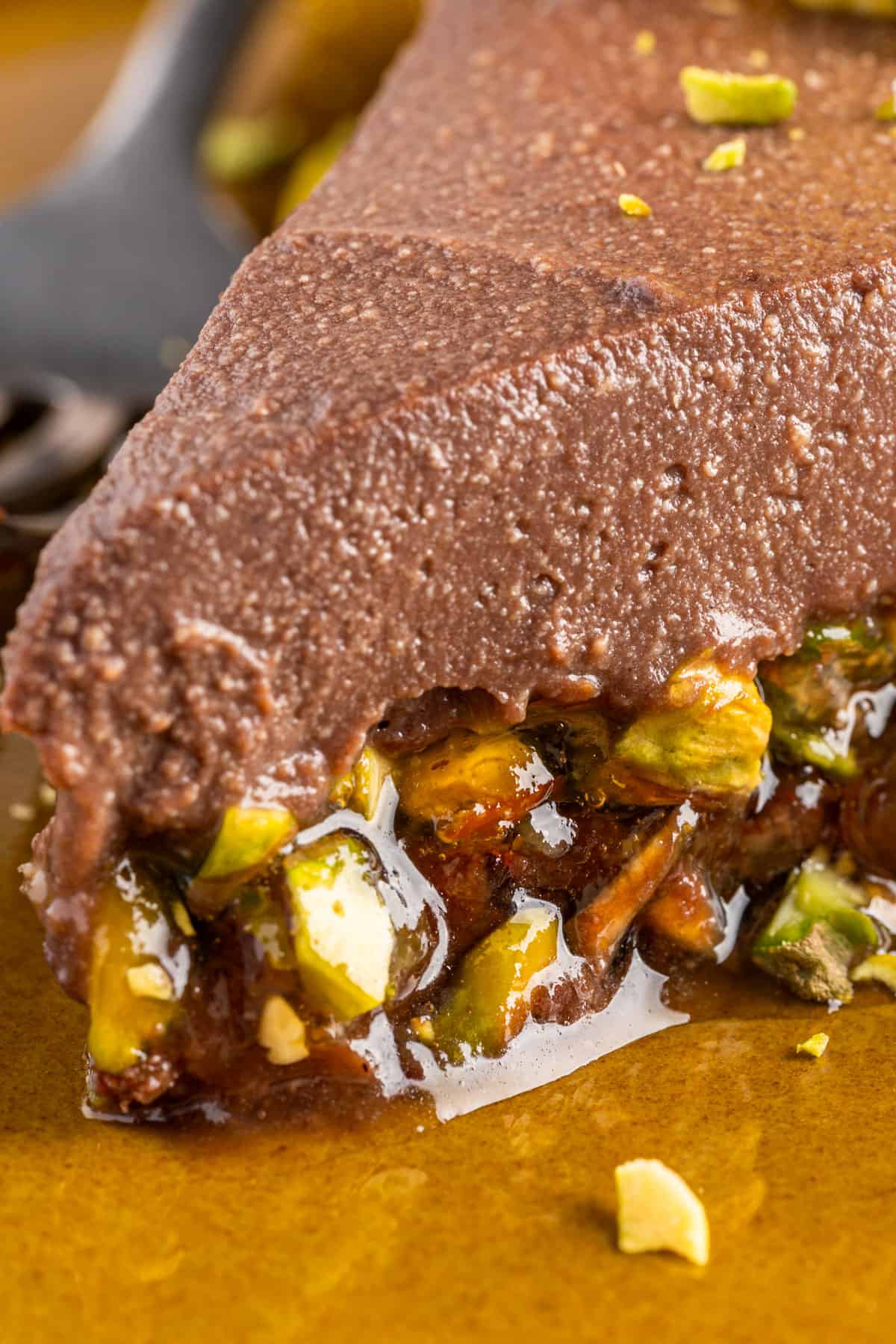 No-Bake Chocolate Tart with Orange Marmalade and Pistachios (Vegan + GF) A close-up photo of a slice of Chocolate Orange Tart on a plate, showcasing the pistachio-orange marmalade and chocolate filling inside the tart.