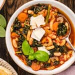Minestrone Soup topped with shaved Parmesan and fresh basil - in a bowl.