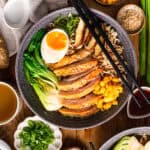 Homemade ramen with jammy egg, shiitake mushrooms, blanched baby bok choy, sweet corn, topped with toasted sesame seeds and green onions - in a bowl.