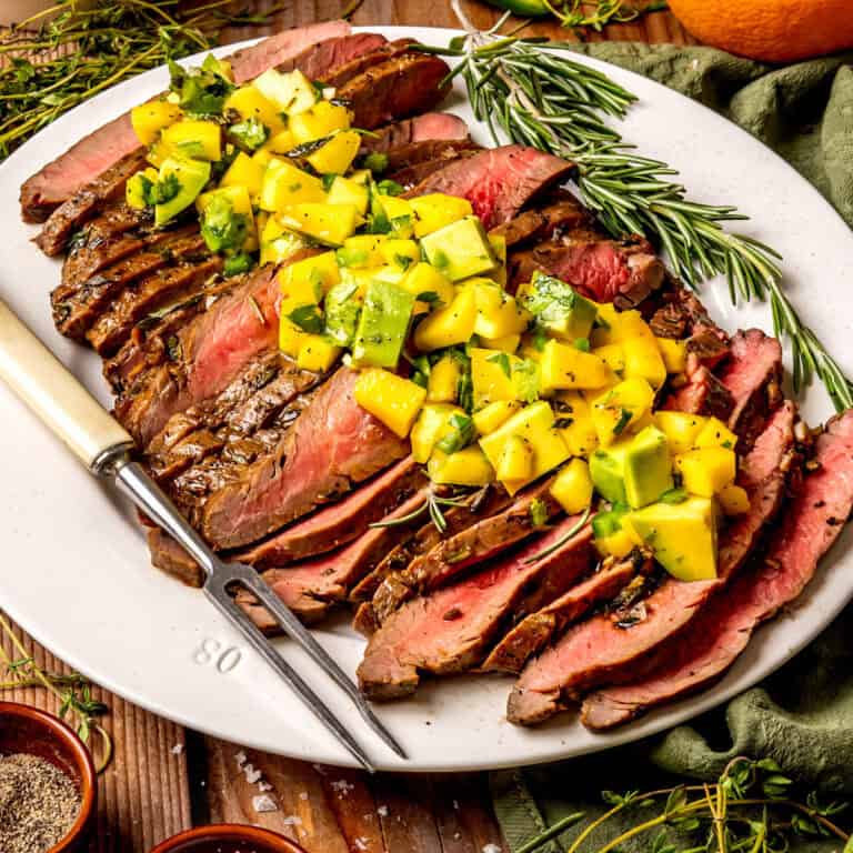 Sliced Grilled Flank Steak topped with Mango-Avocado Salsa on a white plate.