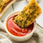 A slice of garlic bread dipped in a red marinara sauce.