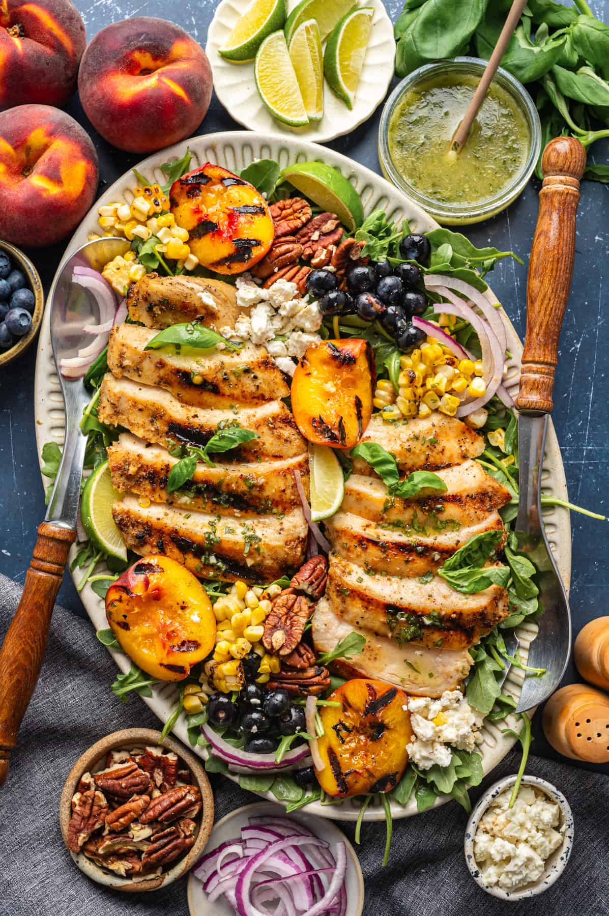 Grilled Chicken and Peach Salad with Lime-Basil Dressing Grilled Chicken and Peach Salad with Corn, Arugula, Blueberries, Feta, Pecans, and Lime Basil Vinaigrette - on a large white platter.