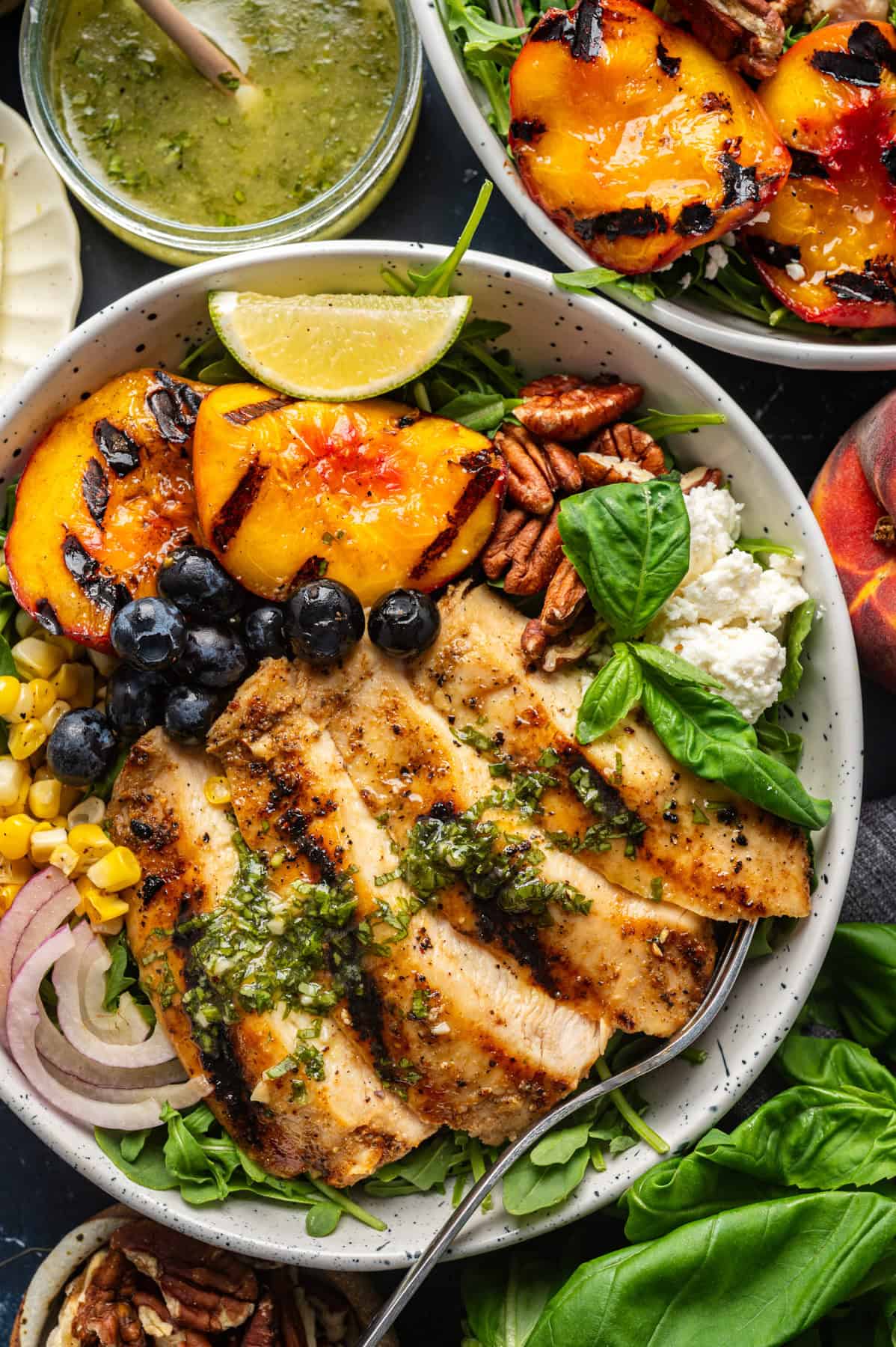 Grilled Chicken and Peach Salad with Lime-Basil Dressing Grilled Chicken and Peach Salad with Corn, Arugula, Blueberries, Feta, Pecans, and Lime Basil Vinaigrette - in a white bowl.
