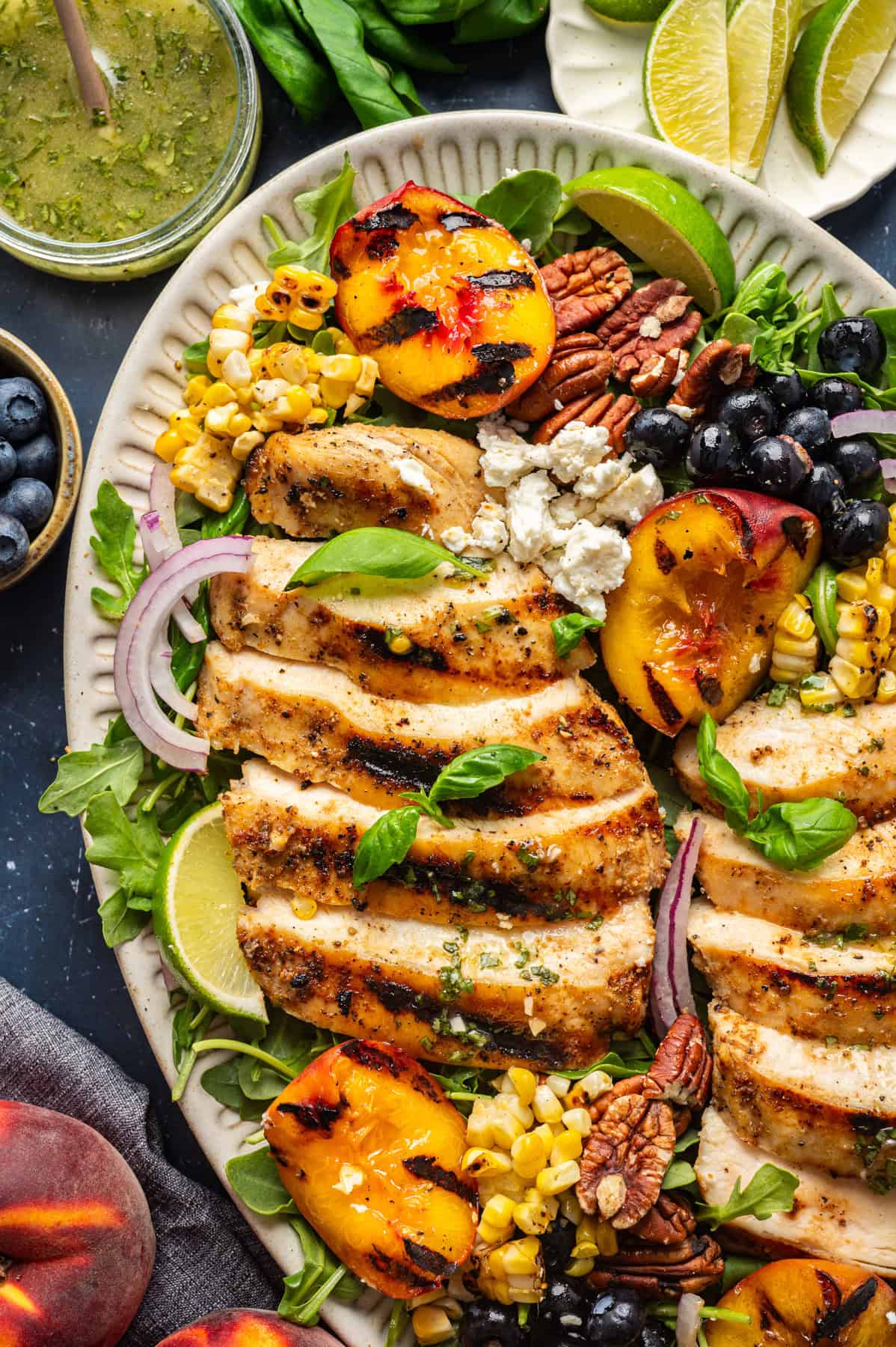 Grilled Chicken and Peach Salad with Lime-Basil Dressing Grilled Chicken and Peach Salad with Corn, Arugula, Blueberries, Feta, Pecans, and Lime Basil Vinaigrette - on a white platter.