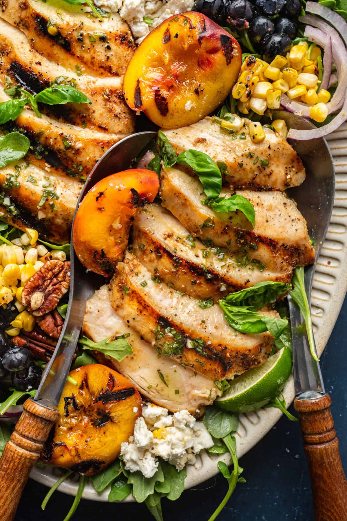 Grilled Chicken and Peach Salad with Lime-Basil Dressing Grilled Chicken and Peach Salad with Corn, Arugula, Blueberries, Feta, Pecans, and Lime Basil Vinaigrette - on a white platter.