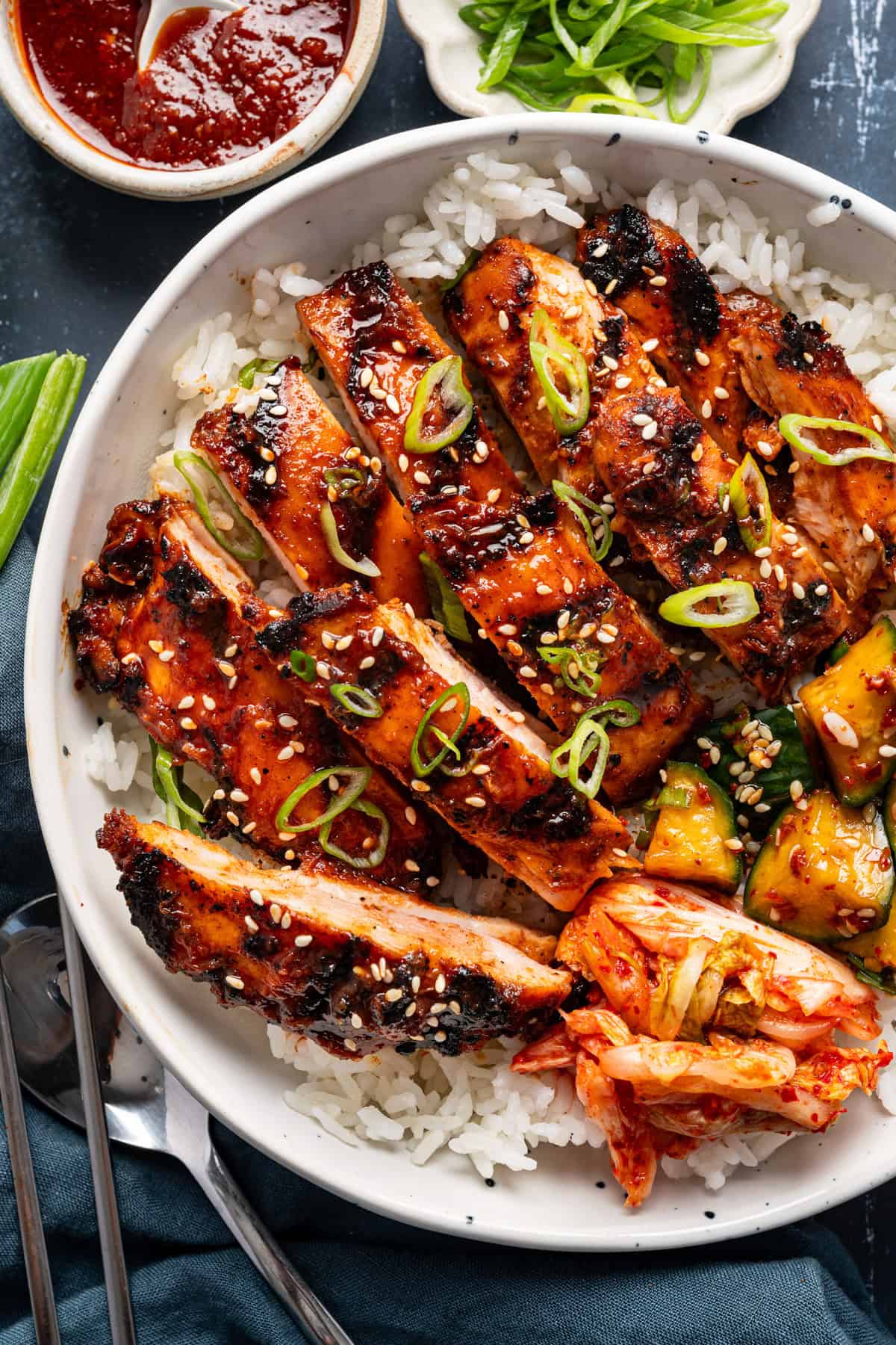 Korean BBQ Chicken with rice, kimchi, and sliced cucumber in a bowl.
