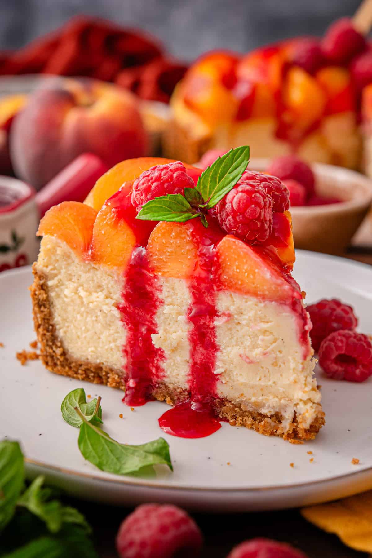 Peach Raspberry Cheesecake A slice of Peach Raspberry Cheesecake drizzled with raspberry sauce on a white plate.