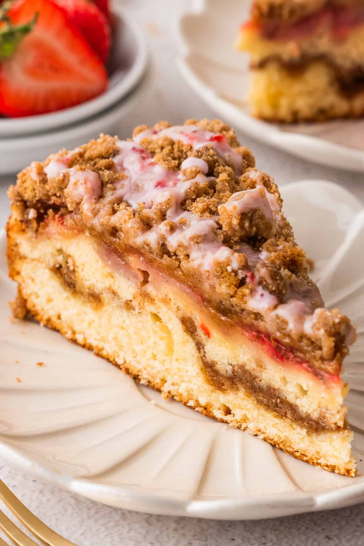 A slice of Strawberry Coffee Cake topped with streusel and pink strawberry glaze - on a white plate.
