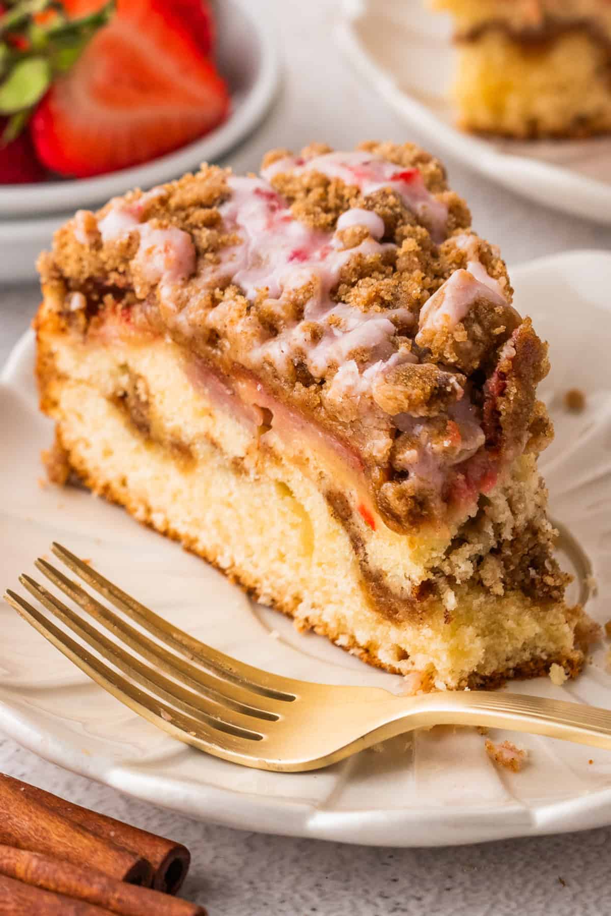 A slice of Strawberry Coffee Cake topped with streusel and pink strawberry glaze - on a white plate with a fork.