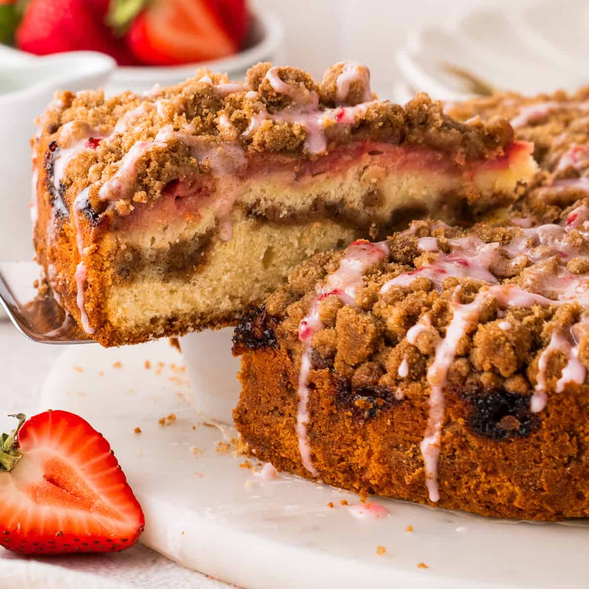 A slice of Strawberry Coffee Cake topped with streusel and pink strawberry glaze being lifted up on a spatula.