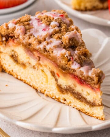 A slice of Strawberry Coffee Cake topped with streusel and pink strawberry glaze - on a white plate.