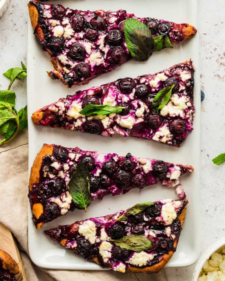Blueberry Feta Flatbread with Mint Leaves - sliced on a white plate.