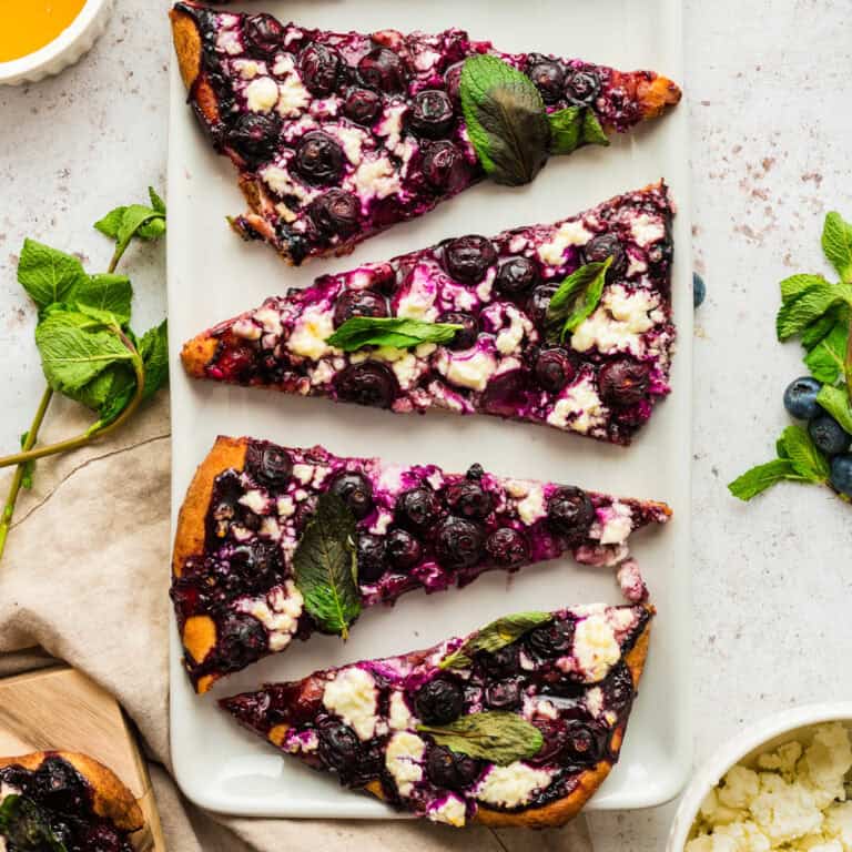 Blueberry Feta Flatbread with Mint Leaves - sliced on a white plate.