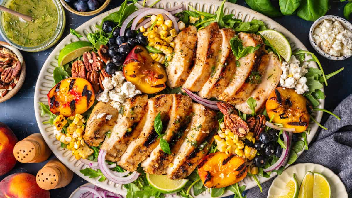 Grilled Chicken and Peach Salad with Corn, Arugula, Blueberries, Feta, Pecans, and Lime Basil Vinaigrette Grilled Chicken and Peach Salad with Corn, Arugula, Blueberries, Feta, Pecans, and Lime Basil Vinaigrette - on a large white platter.