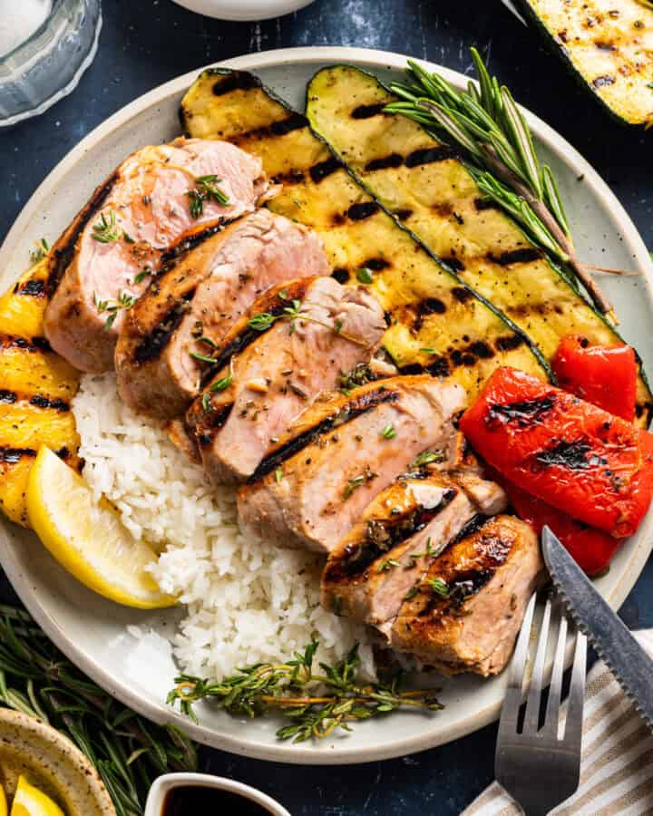 Grilled Pork Tenderloin (sliced) with pineapple slice, grilled veggies (zucchini and bell peppers) and rice - on a white plate.
