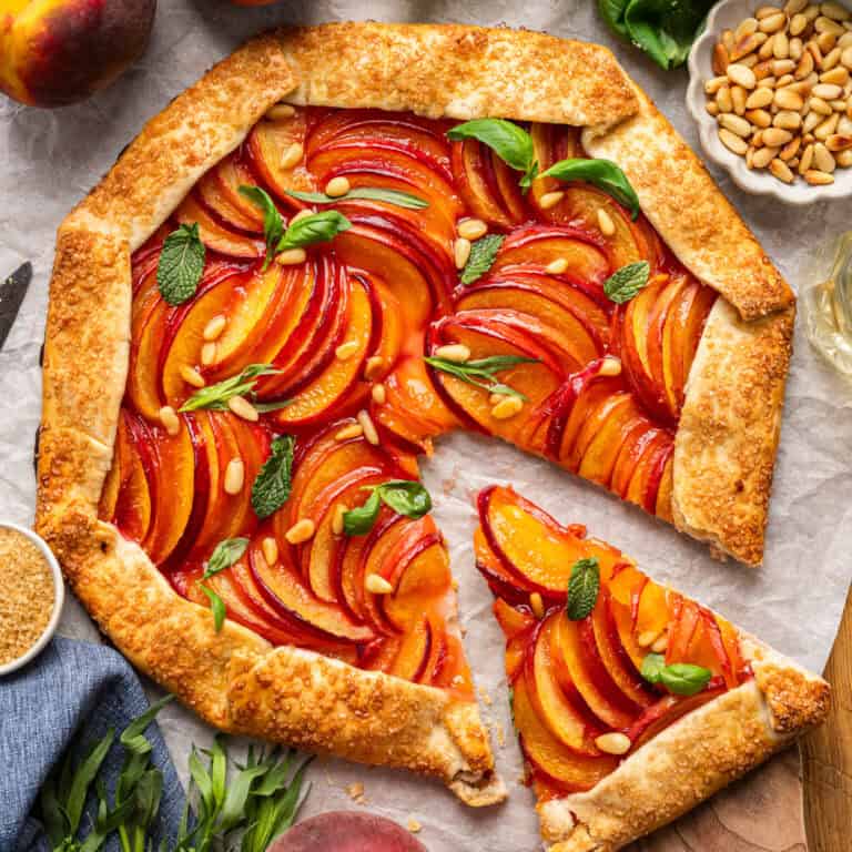 Peach Galette topped with pine nuts, fresh herbs - on white parchment paper.
