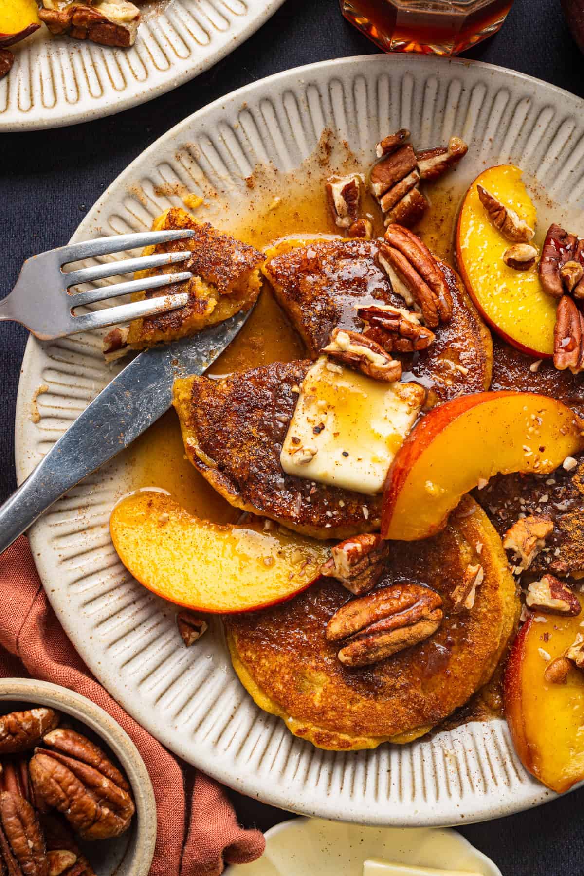 Peach Pancakes with Cinnamon Maple Syrup and Pecans Peach Pancakes with Cinnamon Maple Syrup, Peach Slices, Butter, and Pecans - on a white plate.